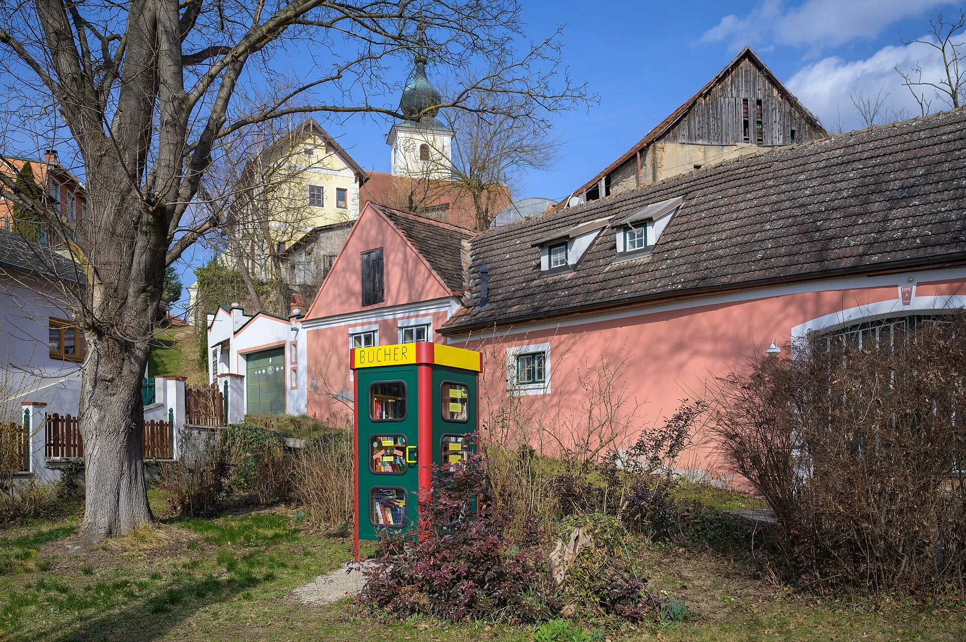 Une boîte à livres de village installée dans une ancienne cabine, devant des maisons colorées